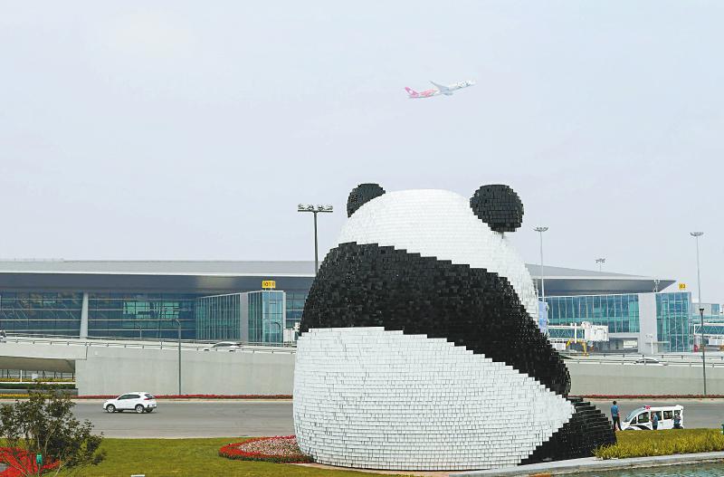 6月27日,首航的川航飞机从成都天府国际机场的大熊猫雕塑"团团"前飞过